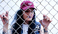 fată purtând o șapcă de baseball care stă în spatele unui gard de zale