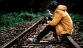 молодой человек сидит на железнодорожных путях и смотрит на фотографии в своей камере