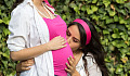 uma jovem beijando a barriga e o feto de sua mãe grávida