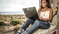 молодая женщина сидит спиной к дереву и работает на своем ноутбуке