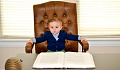 menino sentado em uma grande cadeira de couro em frente a uma mesa de negócios