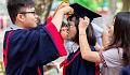 Dos estudiantes ajustando el birrete de graduación de otro.