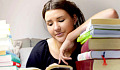 a young woman peacefully reading a book with her arm resting a whole stack of books