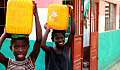 Two joyful African children carrying buckets of water on their head