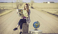 一位年轻女子坐在路中间的手提箱上，旁边有一个地球仪