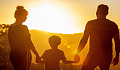 sepasang suami isteri memegang tangan anak mereka menghadap matahari terbenam