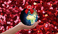 una mano sosteniendo el Planeta Tierra rodeada de corazones