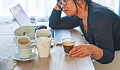 een vrouw die er gestresst en moe uitziet terwijl ze een kopje koffie drinkt en omringd is door meerdere kopjes leeg en vol