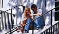 sepasang suami istri duduk di tangga luar sambil memandangi ponsel mereka