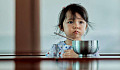 unhappy child sitting in front of a bowl of food