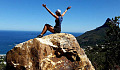 турист сидит на вершине огромной скалы с триумфально поднятыми руками