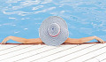 婦女躺在游泳池裡，她的手臂在邊緣，戴著太陽帽
