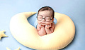 کودکی با چشمان بسته که عینک بزرگی به چشم دارد و روی بالش هلال ماه قرار گرفته است