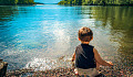 young child sitting at the edge of a peaceful lake