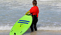 kind dat aan de rand van de oceaan staat en een surfplank vasthoudt