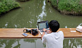 egy fiatal fiú a hajón nyitott laptoppal, mellette fényképezőgéppel és mobiltelefonnal.