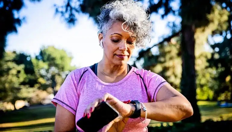 O femeie își verifică ceasul inteligent în timp ce se plimbă prin parc