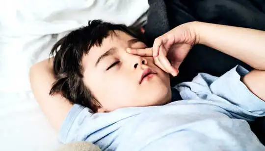 ילד צעיר משפשף את עינו כשהוא נשכב במיטה