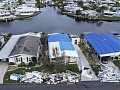 A flood-swollen canal is menacingly visible behind a row of hurricane-battered houses.