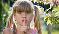 a young girl with her finger over her mouth in the universal symbol of "hush, be quiet"