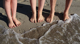 เท้าคู่ยืนอยู่บนชายหาดที่ขอบคลื่นที่เข้าฝั่ง