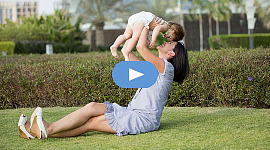 leende mamma, sitter på gräset, håller upp ett barn