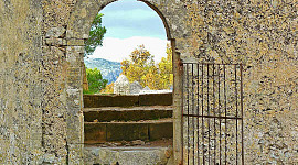 Otwarta brama w kamiennym murze, otwierająca się na piękną scenerię przyrody.