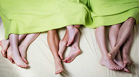 The bare feet and lower legs of three couples laying under the same lime green blanket.