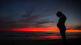 en gravid kvinne i silhuett med soloppgangen i bakgrunnen