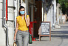 nainen kävelee kadulla yllään naamio ja koskettaa kasvojaan