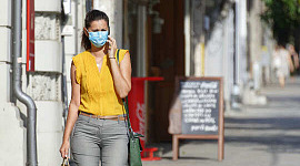 donna che cammina per strada indossando una maschera e toccandosi il viso