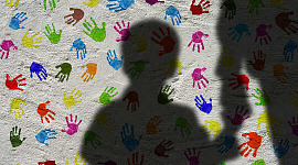 silhuett av en gutt som holder en voksens hånd, med en bakgrunn av fargerike håndtrykk på veggen