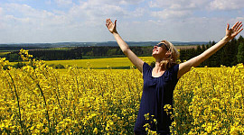 women standing in a field of flowers, smiling with her hands open up to the sky