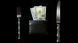 uma mesa posta com uma faca e um garfo e uma carteira cheia de dinheiro onde o prato normalmente estaria