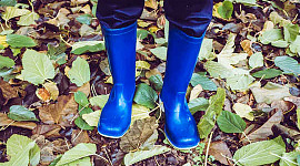 孩子的腳穿著藍色橡膠靴，地上有樹葉的照片