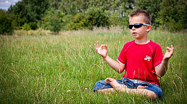 băiat tânăr purtând ochelari de soare meditând pe un câmp deschis