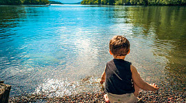 शांत झील के किनारे बैठा छोटा बच्चा