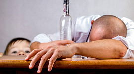 seorang lelaki terbaring di atas meja dengan sebotol alkohol kosong dengan anak yang sedang melihat