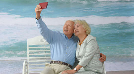 Pareja de ancianos canosos sentado en un banco en la playa tomando un selfie