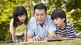 دو بچے اپنے والد کے ساتھ کتاب پڑھ رہے ہیں