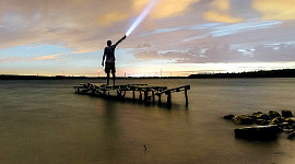 Mann steht auf einem Dock und leuchtet mit einer Taschenlampe in den Himmel
