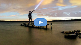 Mann steht auf einem Dock und leuchtet mit einer Taschenlampe in den Himmel