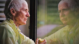 ältere Person, die einen Apfel isst und ihr Spiegelbild in einem Fenster betrachtet