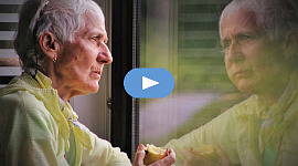 eldre person spiser et eple og ser på refleksjonen hennes i et vindu