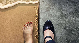 Chế độ xem tách đôi của 2 bàn chân: 1 người đi chân trần trên bãi biển, người còn lại đi giày cao gót màu đen trên sàn bóng