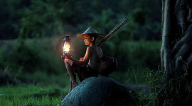 niño sentado afuera con una linterna, esperando el amanecer