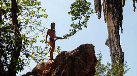 um menino escalando até o topo de uma formação rochosa