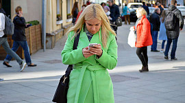 nainen kadulla katselee tarkasti puhelintaan