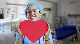 glimlachende verpleegster die een papier omhoog houdt dat in een hartvorm is uitgesneden