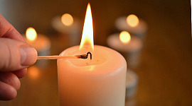 a hand lighting a candle, with other lit canndles in the background